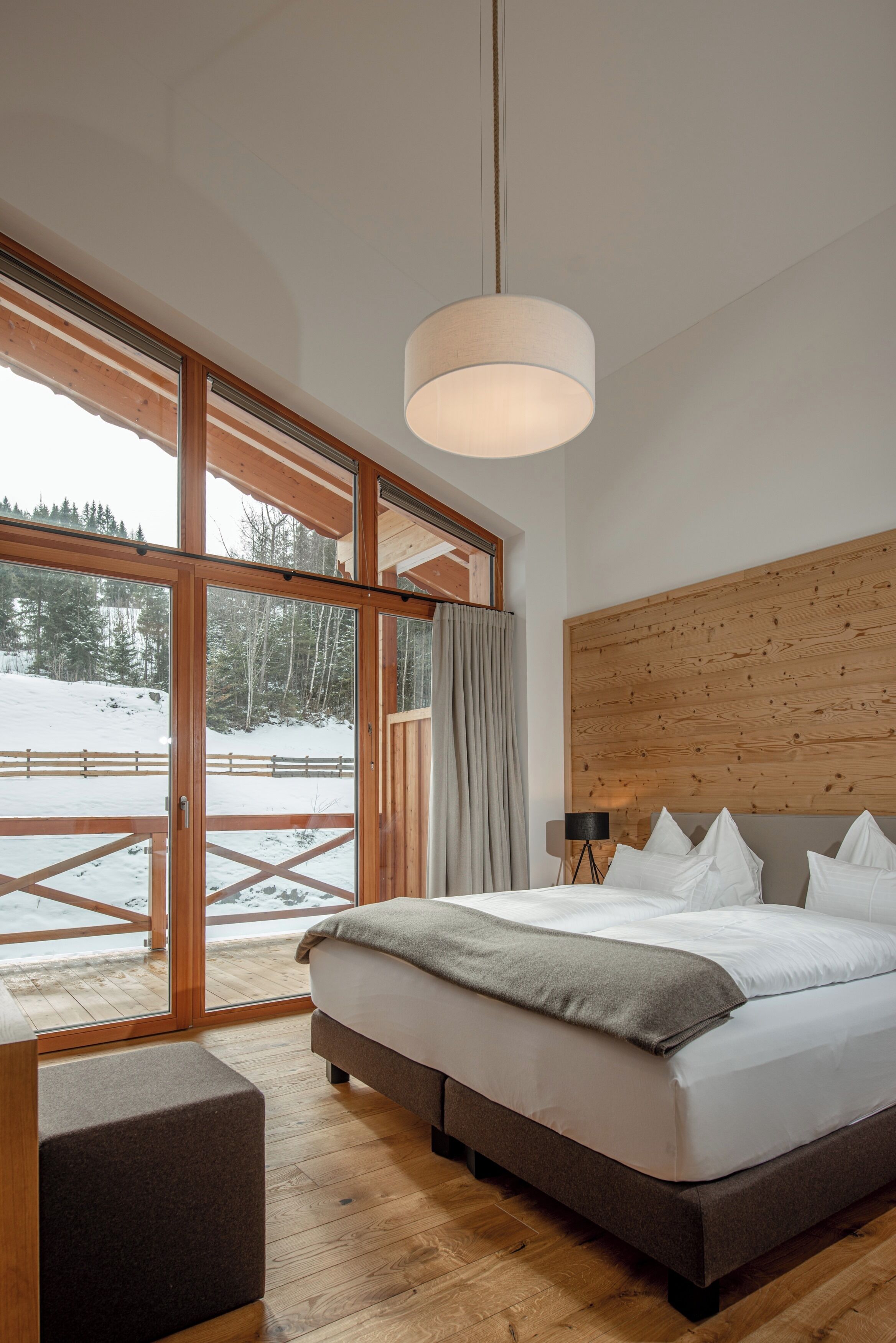 Un dormitorio con una ventana grande, una cama, una mesita de noche y una lámpara.