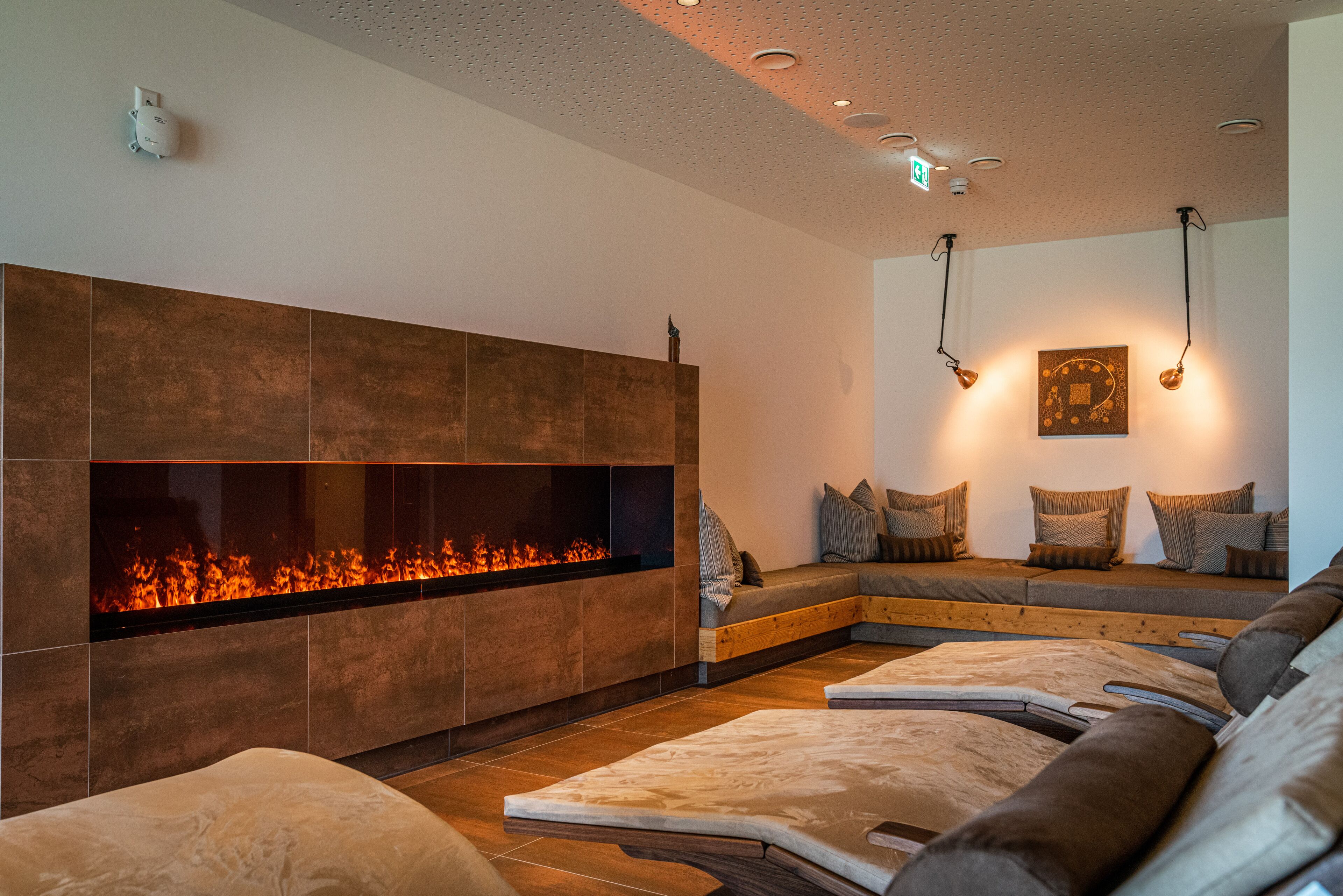 A modern lounge area with a built-in fireplace, seating with cushions, and pendant lighting.