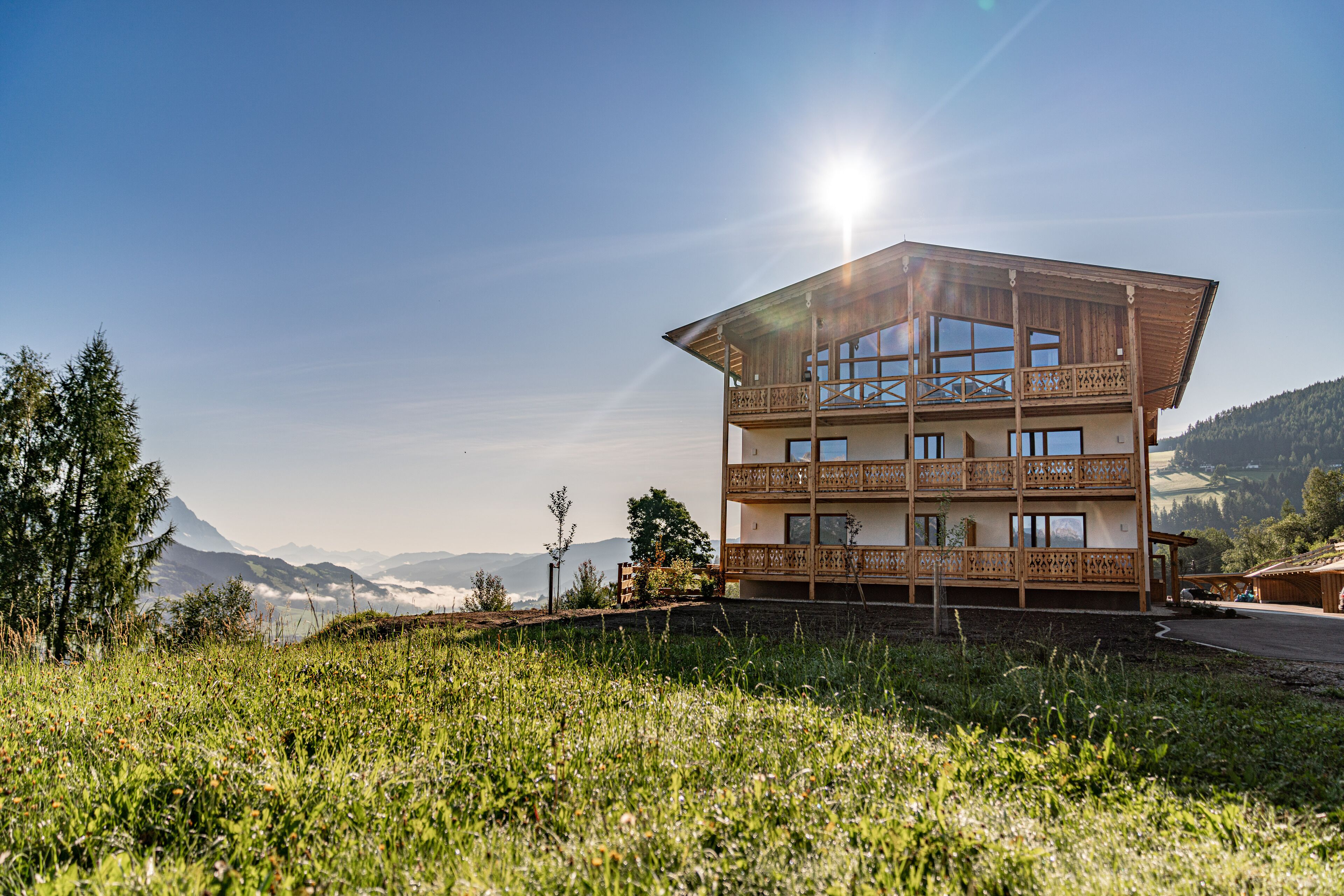A multi-story chalet with balconies, set in a mountainous area with a clear sky.