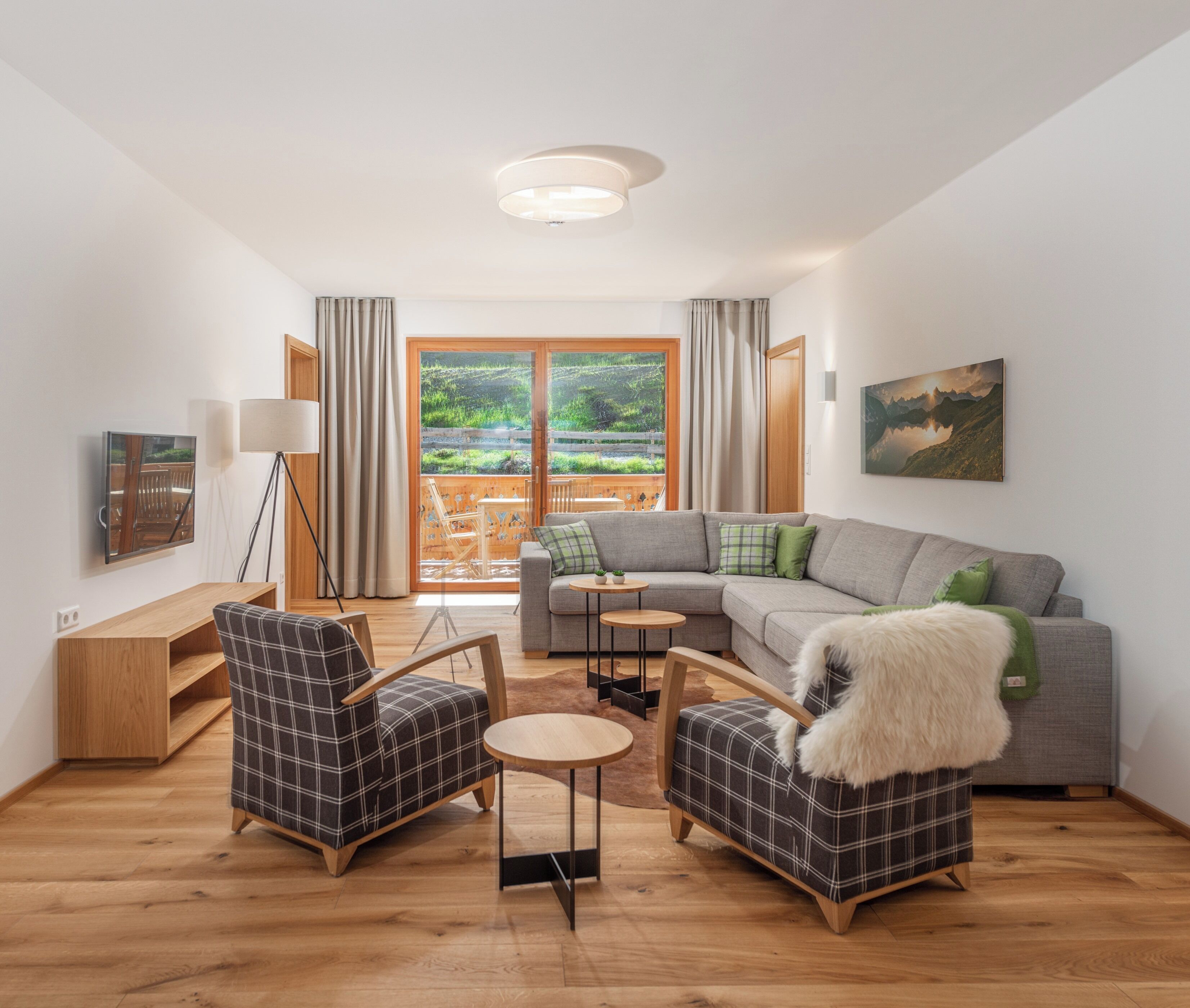 A modern living room with a grey sofa, two plaid armchairs, a small round table, and a wooden floor.