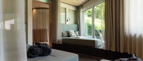 A modern hotel room with a large window, a sofa bed, and a view of greenery outside.