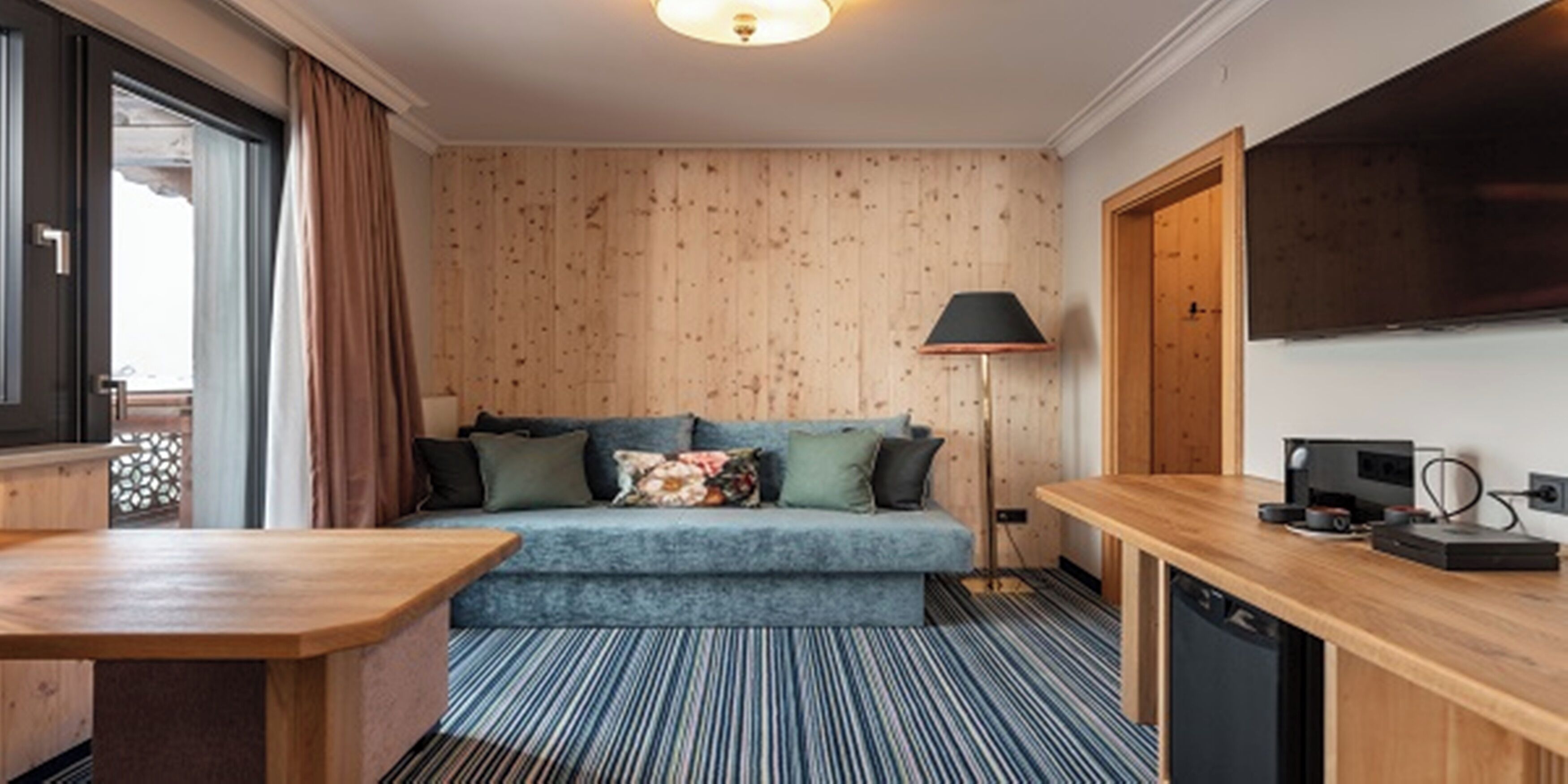 A cozy room with a blue sofa, a wooden desk, a lamp, and a television.