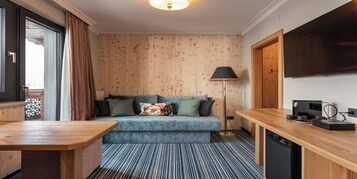 A cozy room with a blue sofa, a wooden desk, a lamp, and a television.