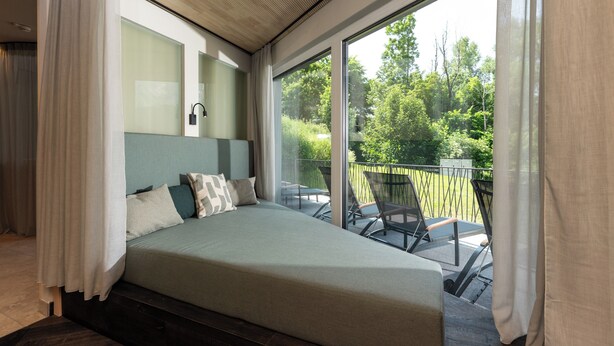 Een slaapkamer met een groot bed, uitzicht op de natuur en een balkon met stoelen.