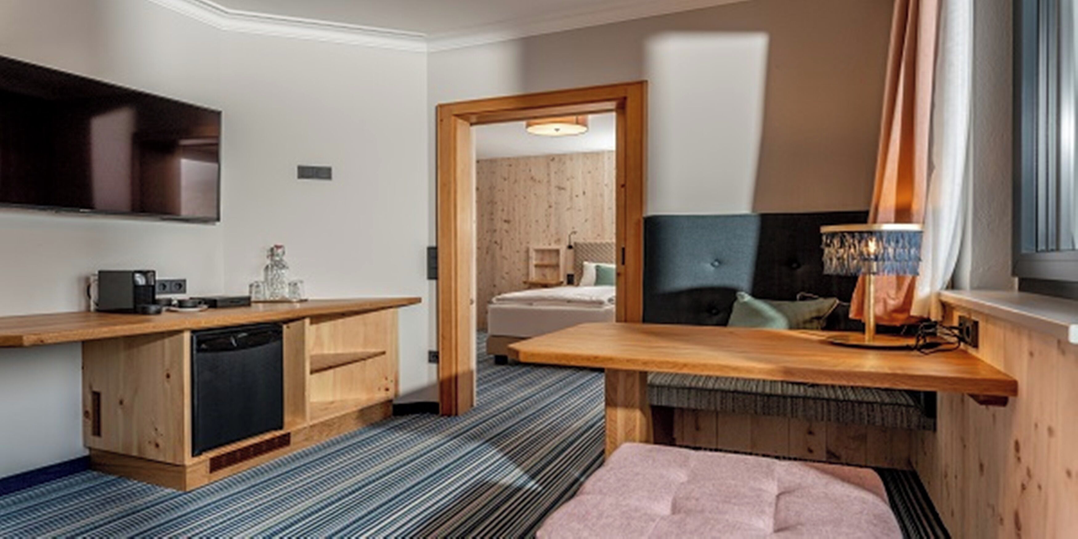 Una habitación de hotel compacta con kitchenette, una cama, un televisor y un ventanal con cortinas.