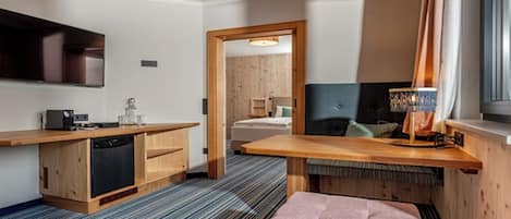 Una habitación de hotel compacta con kitchenette, una cama, un televisor y un ventanal con cortinas.