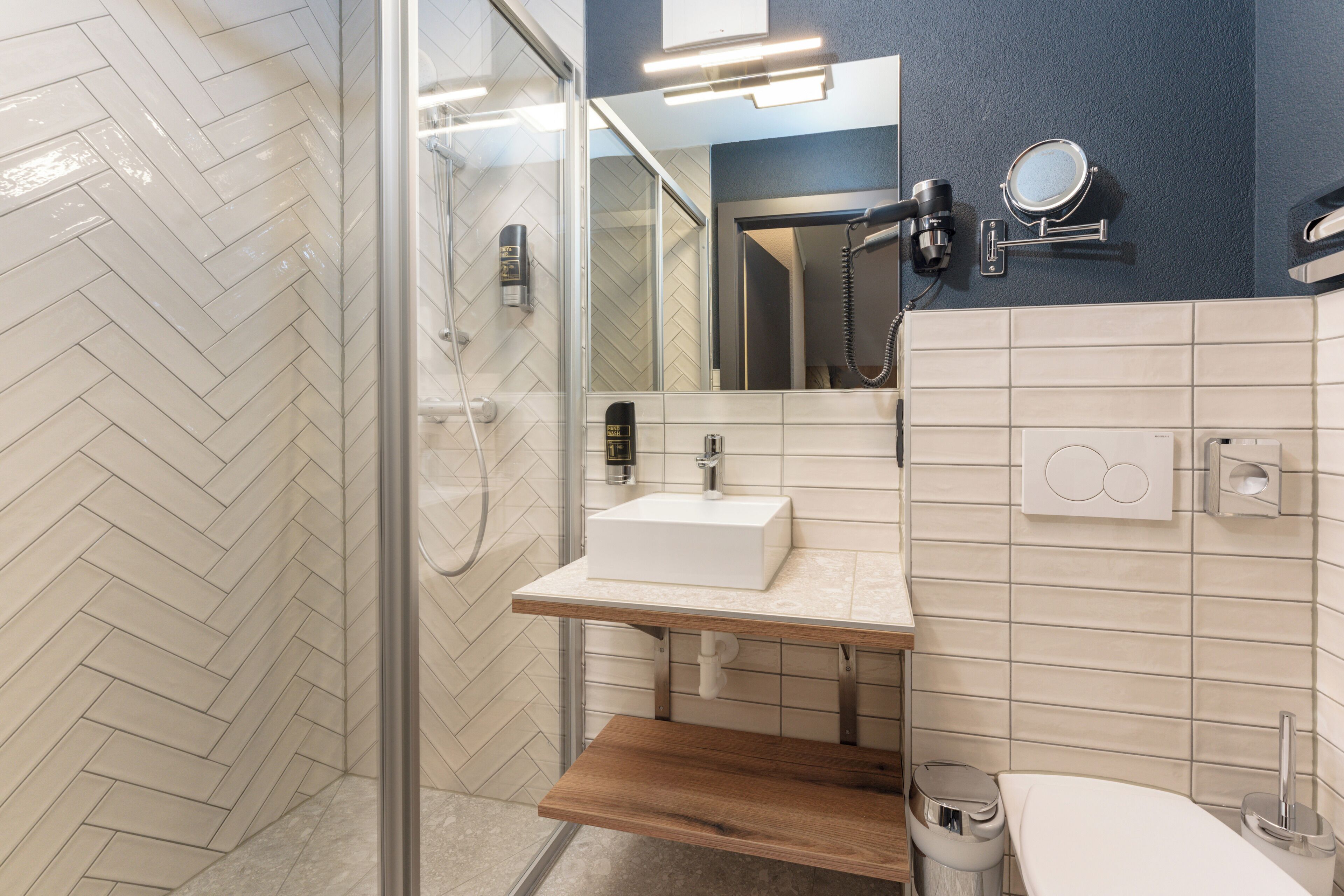 Un baño moderno con cabina de ducha de vidrio, tocador de madera con lavamanos blanco y espejo sobre el lavamanos.