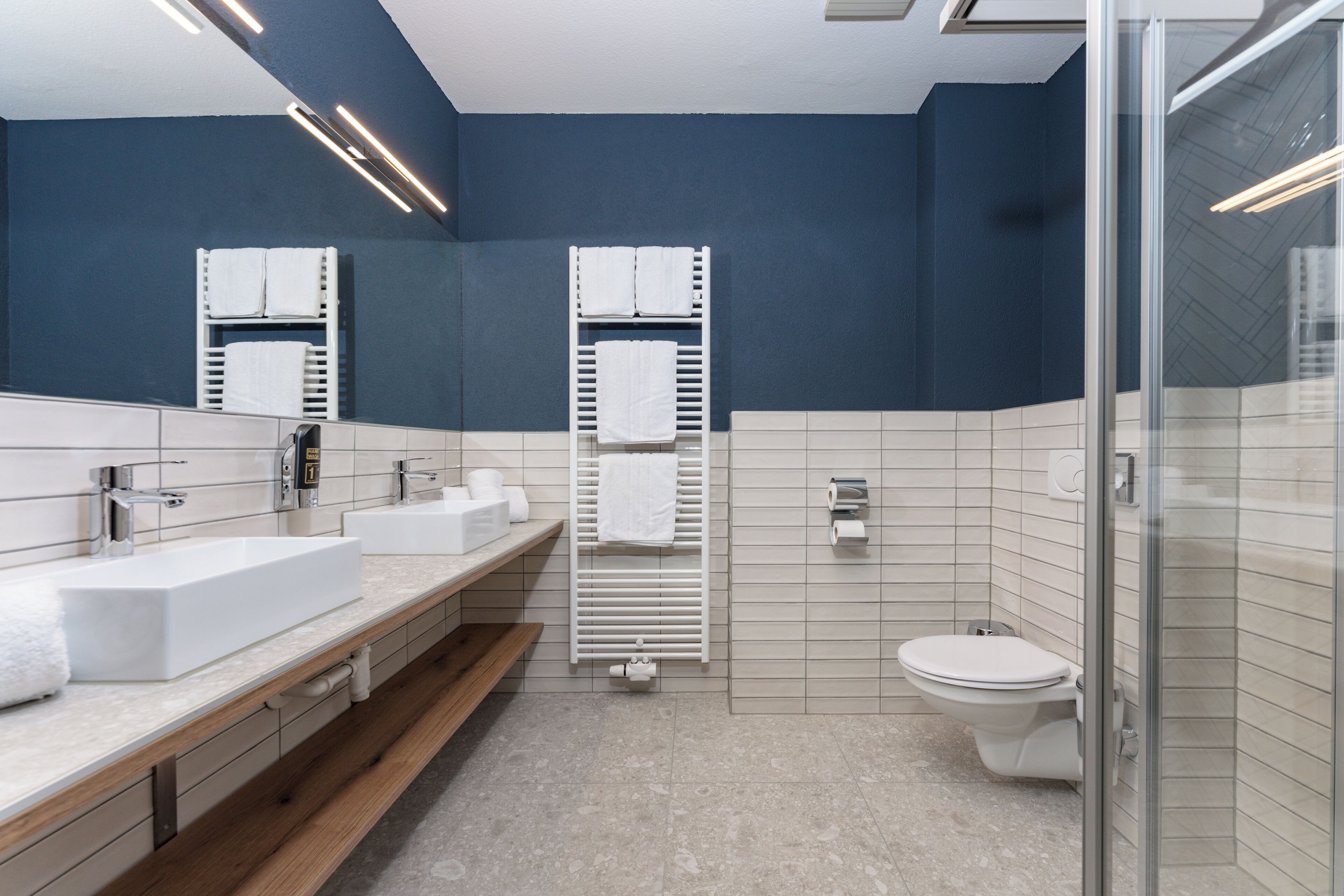 A modern bathroom with two sinks, a toilet, and a glass shower enclosure.