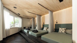 Een moderne hotelkamer met een houten plafond, grote ramen met gordijnen, een visgraatvloer en een bed met een groen hoofdeinde.