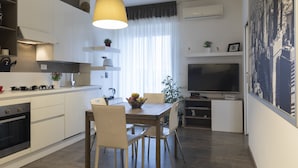 Uma cozinha moderna com armários brancos, uma mesa de jantar com cadeiras, um lustre e uma grande TV de tela plana.