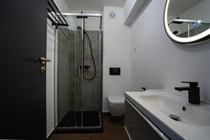 Uma casa de banho moderna com chuveiro envidraçado, lavatório branco e sanita.