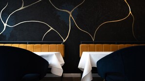 Interior de restaurante com dois reservados e mesas, apresentando uma parede escura com um design abstrato dourado.