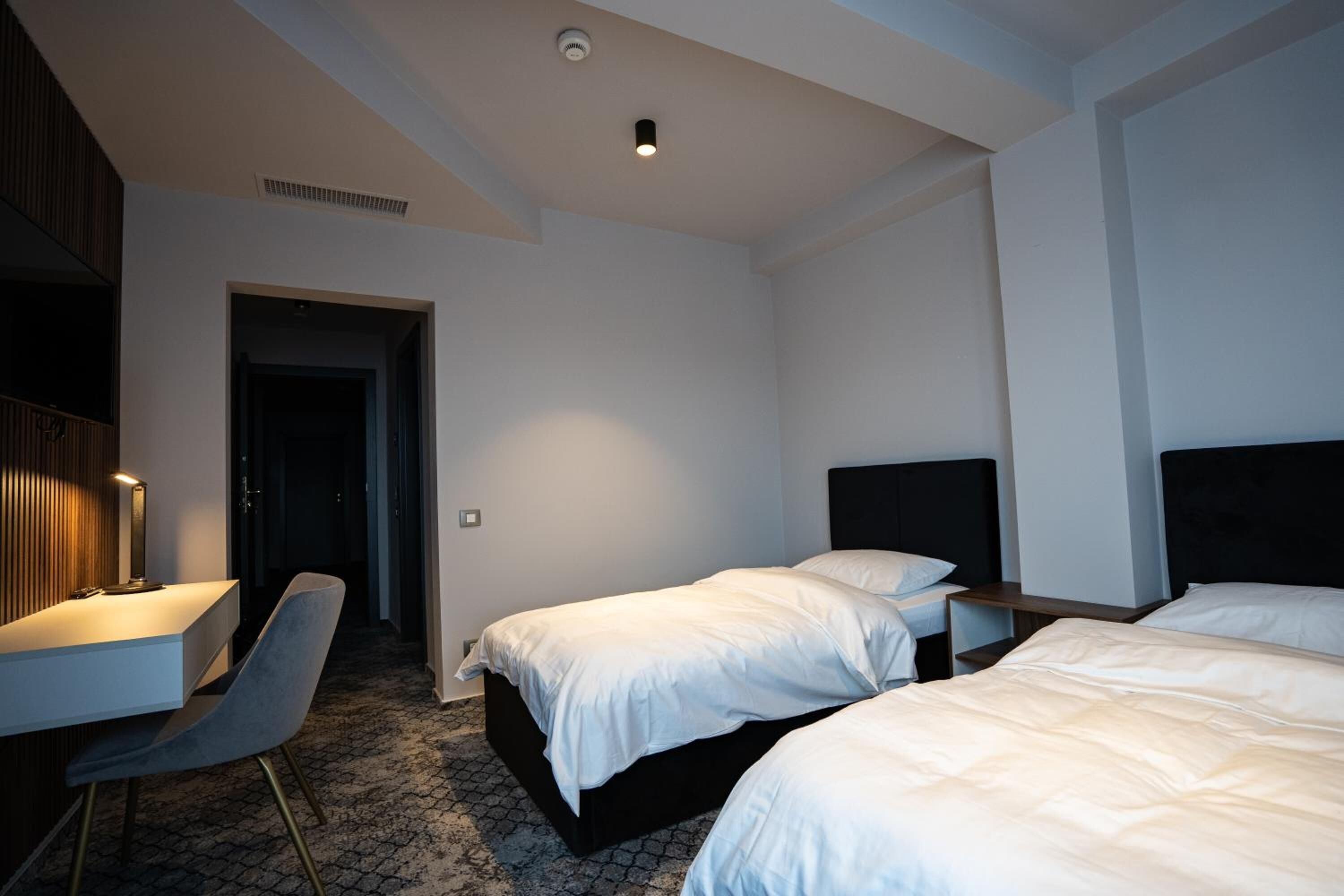 A hotel room with two beds, a desk, a chair, and a door leading to a hallway.