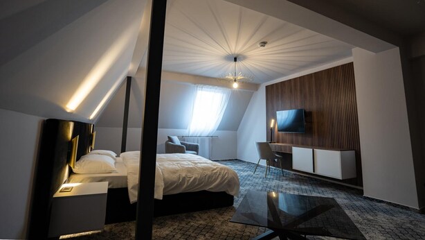 Quarto de hotel moderno com cama, mesa de cabeceira, escrivaninha, cadeira, TV e um design de teto exclusivo.
