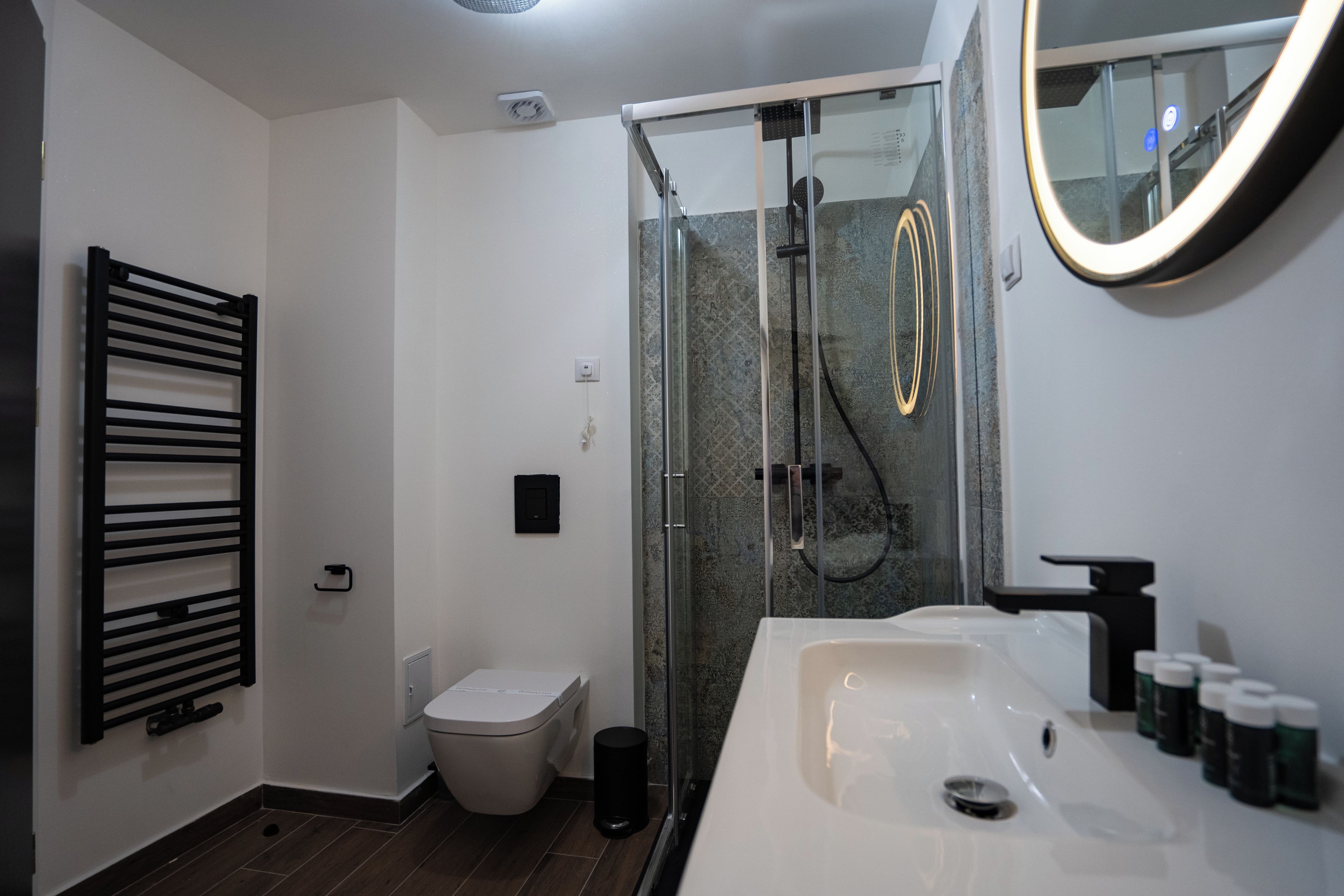 Un baño moderno con ducha de vidrio, un lavamanos blanco con grifo negro y un toallero negro.