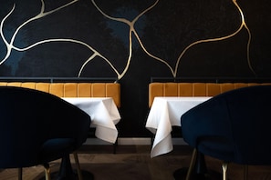 A restaurant interior with two tables, dark chairs, and a wall with abstract gold lines. - Cristal Hotel (Cluj-Napoca)
