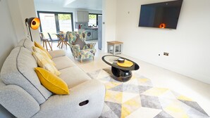 A modern living room with a grey sofa, yellow cushions, a patterned rug, a coffee table, and a TV mounted on the wall. - Newly Refurbished 4 Double Bed House with Parking (Slough)