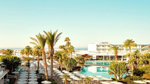 A resort with a pool surrounded by palm trees and lounge chairs. - Sunwing Sandy Bay Beach (Ayia Napa)