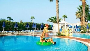 A swimming pool with a giraffe float, palm trees, and lounge chairs with umbrellas. - Sunwing Sandy Bay Beach (Ayia Napa)
