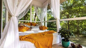 A bedroom with a canopy bed, white bedding, and a view of a forest. - Lakefront Escape|Fireplace+Paddleboard+Hottub (North Liberty)