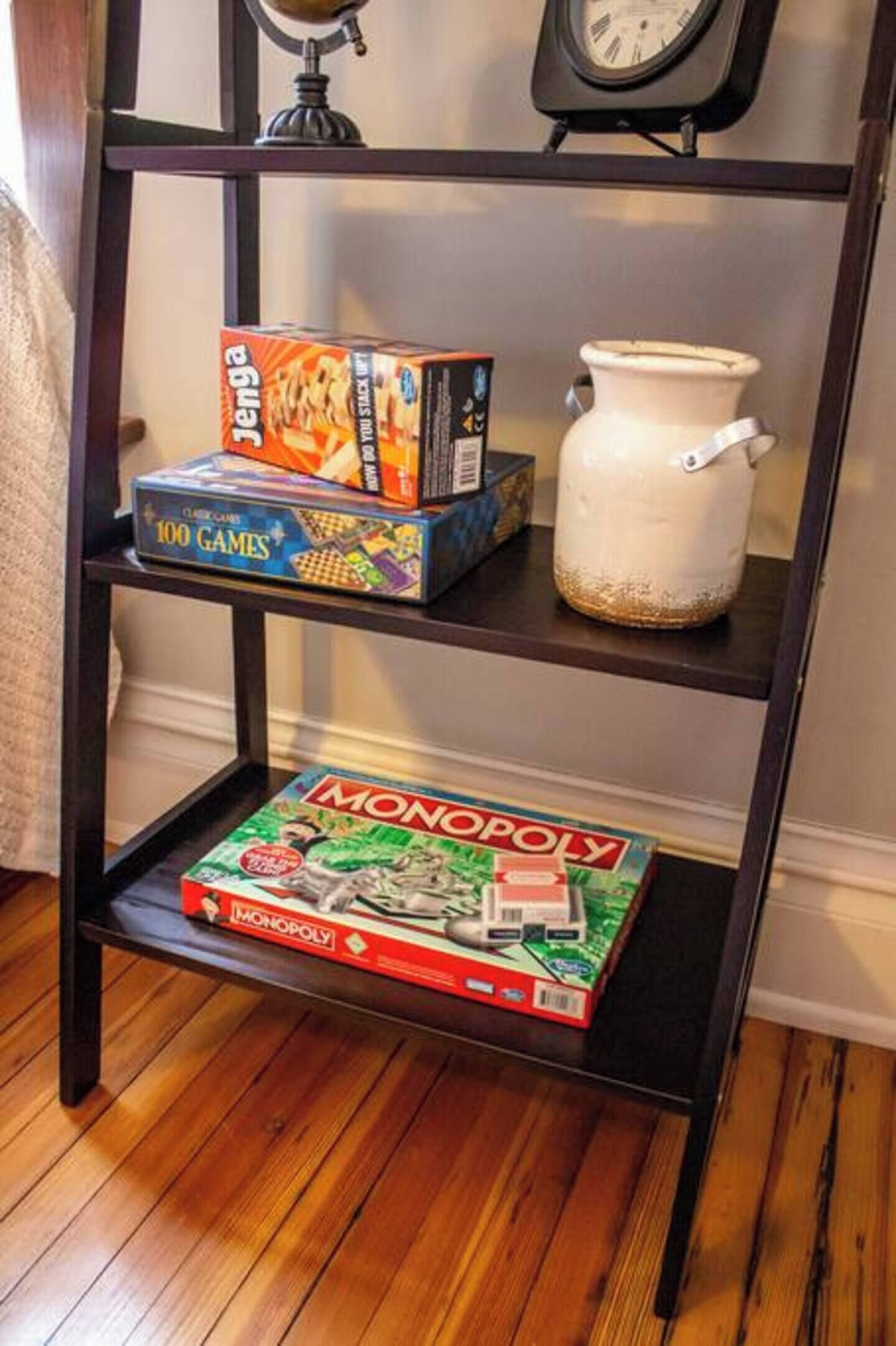 A shelf with a Monopoly board game, a Jenga box, and a white ceramic pot.