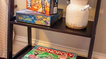 A shelf with a Monopoly board game, a Jenga box, and a white ceramic pot.