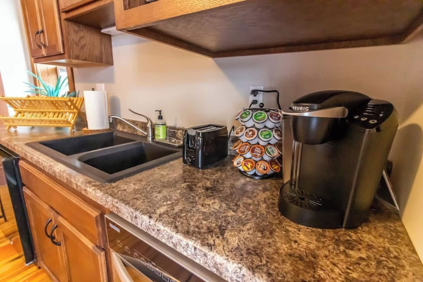 A kitchen with granite countertops, a coffee maker, a toaster, and a dish rack with multiple bowls.
