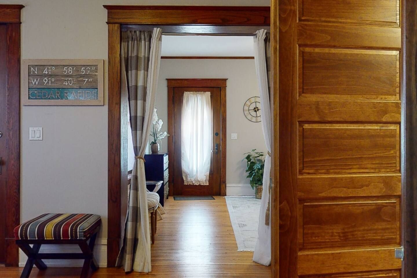 Un couloir avec une porte en bois, un banc, un panneau indiquant des coordonnées et une plante.