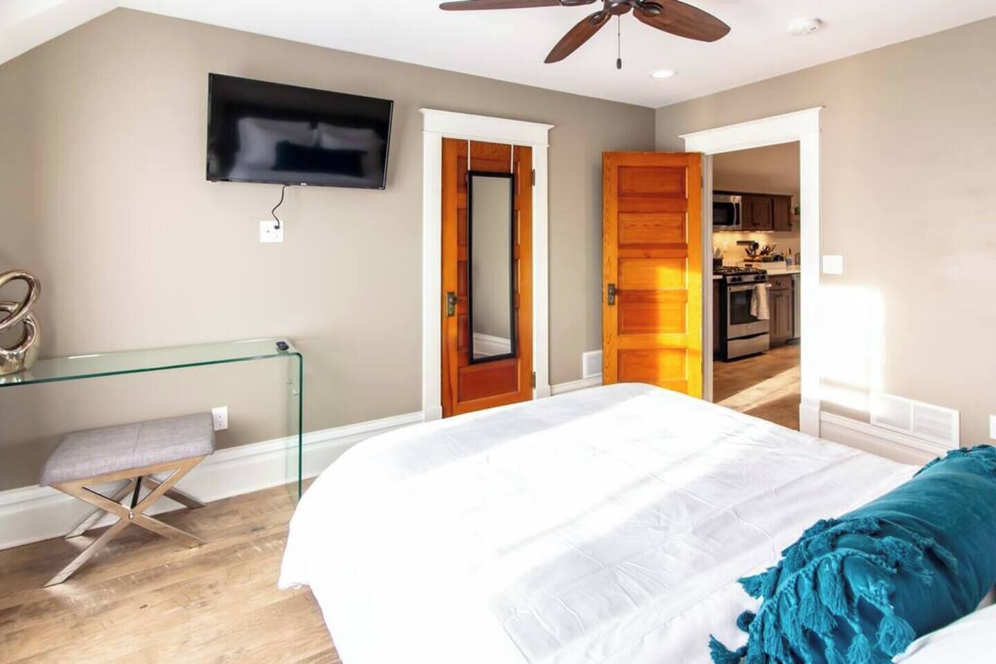 Un dormitorio con cama, escritorio de vidrio, televisor y ventilador de techo.