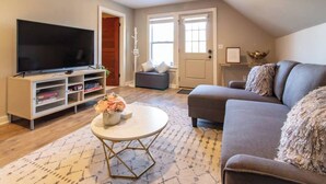 A living room with a flat-screen TV, a grey sofa, a coffee table, and a bookshelf. - Best Location in town!!! Steps from coffee, bars, shops, river and Czech  - Pets ! Arcade (Cedar Rapids)