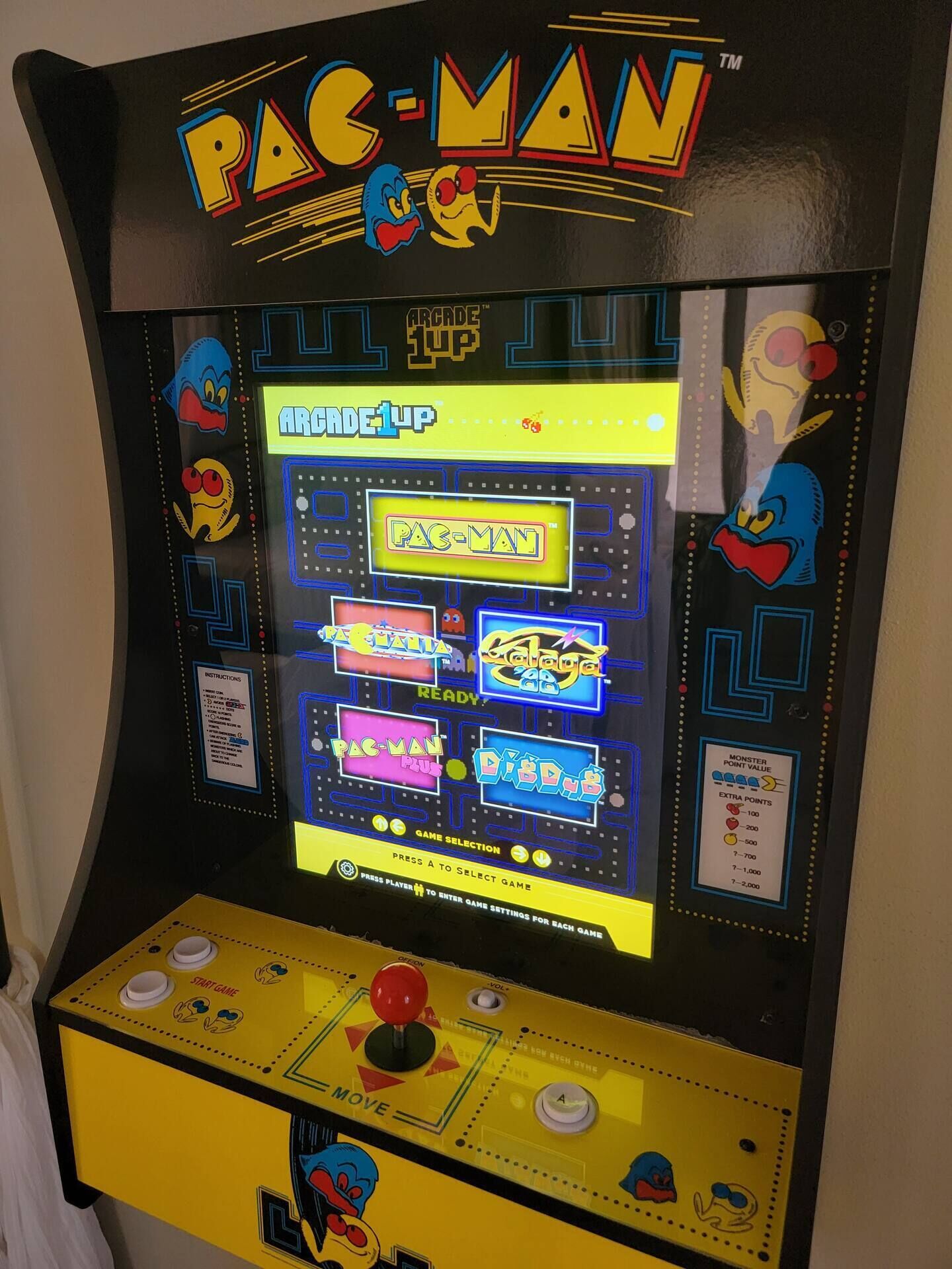 Máquina de arcade Pac-Man com painel de controle amarelo e tela de seleção de jogo.