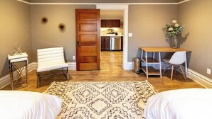A hotel room with a bed, a white chair, a desk, a small table, a rug, and a door leading to a kitchen area. - Best Location in town!!! Steps from coffee, bars, shops, river and Czech  - Pets ! Arcade (Cedar Rapids)