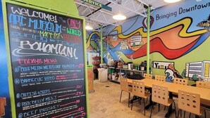 A restaurant with a chalkboard menu listing items like 'Bohemian Meatloaf Burger' and 'Barbecue Ribs'. The walls are decorated with colorful murals depicting city scenes and a butterfly. - Best Location in town!!! Steps from coffee, bars, shops, river and Czech  - Pets ! Arcade (Cedar Rapids)