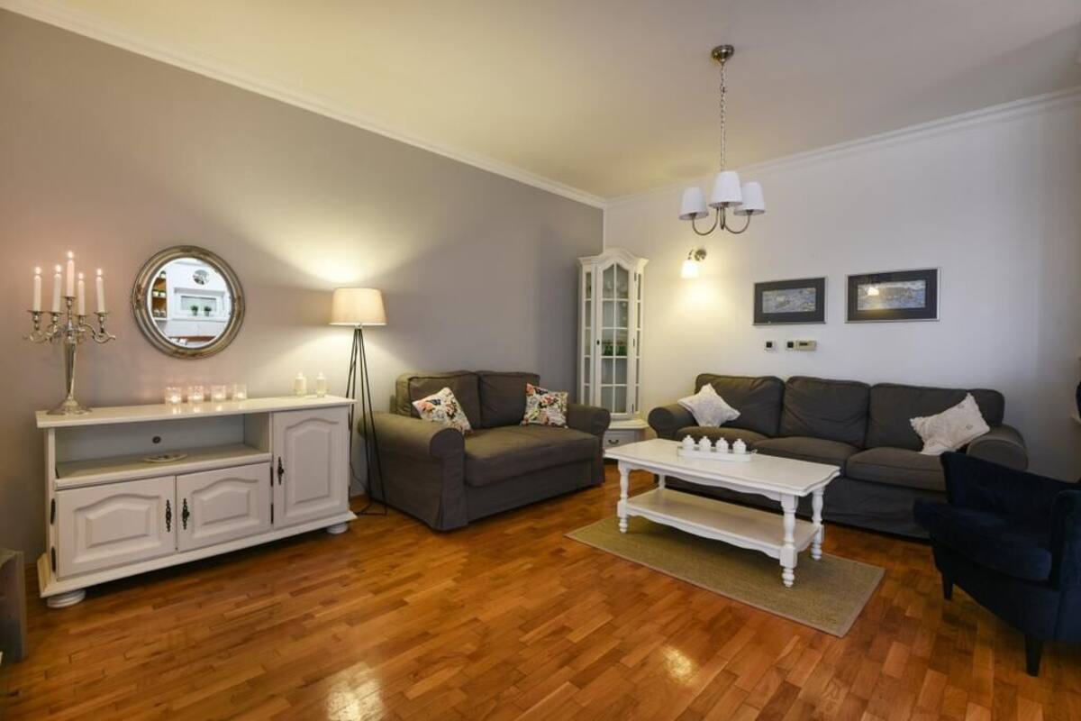 A living room with a grey sofa, a white coffee table, a white cabinet, and a mirror on the wall.