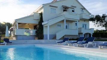 A two-story building with a swimming pool, lounge chairs, and a staircase leading to the upper floor.