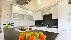 Une cuisine moderne avec des meubles blancs, un plan de travail noir et un panier de fruits contenant des oranges et des pommes.