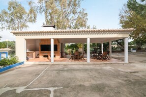 Un espacio al aire libre techado con una parrilla, asientos y vista a árboles.