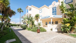 A hotel with a cobblestone driveway, palm trees, and a sign with a 'G' on the building.