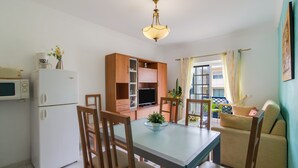 A compact living space with a dining table, chairs, a sofa, a TV, a microwave, and a refrigerator.