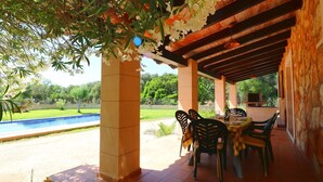 Un espacio al aire libre techado con piscina, mesa de comedor, sillas y una pérgola adornada con flores.