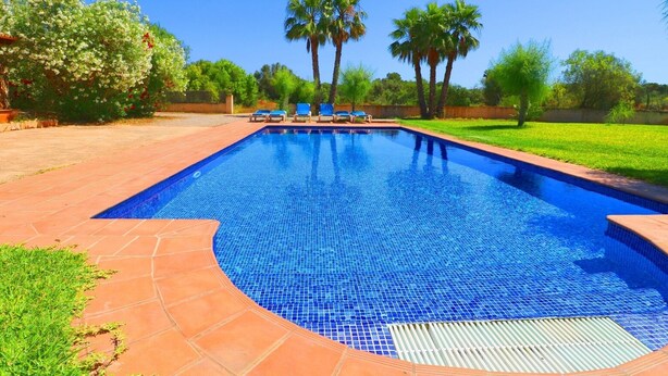 Piscina rectangular con borde de azulejos, rodeada por un patio con piso de baldosas y césped.