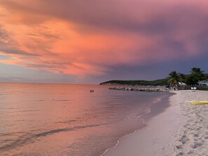 A beach with a rocky breakwater, calm sea, and a sunset sky.