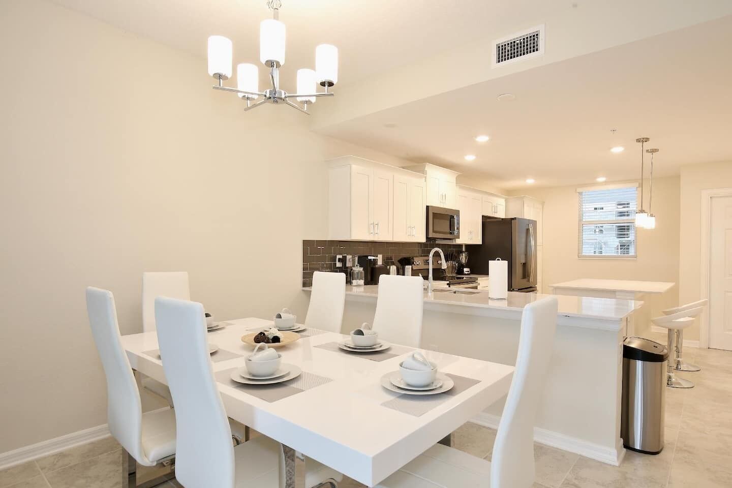 A modern kitchen with white cabinetry, a central island, and a dining area with white chairs and a table set for four.
