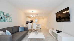 A modern living room with a grey sofa, white coffee table, and a TV mounted on the wall. - New high end apartment  in luxurious Storey Lake community. Next to Disney! (Kissimmee)