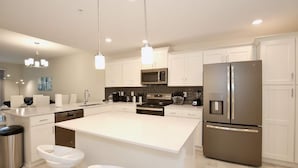 A modern kitchen with white cabinetry, stainless steel appliances, and a central island with bar stools. - New high end apartment  in luxurious Storey Lake community. Next to Disney! (Kissimmee)