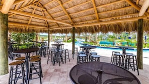 An outdoor patio area with thatched roof seating and tables, overlooking a swimming pool. - New high end apartment  in luxurious Storey Lake community. Next to Disney! (Kissimmee)