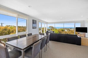 A modern living room with a large dining table, comfortable seating, a flat-screen TV, and a scenic ocean view. - View Point (Anglesea)