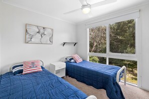 A bedroom with two beds, a ceiling fan, a nightstand, a window with a view of trees, and a wall-mounted shelf. - View Point (Anglesea)