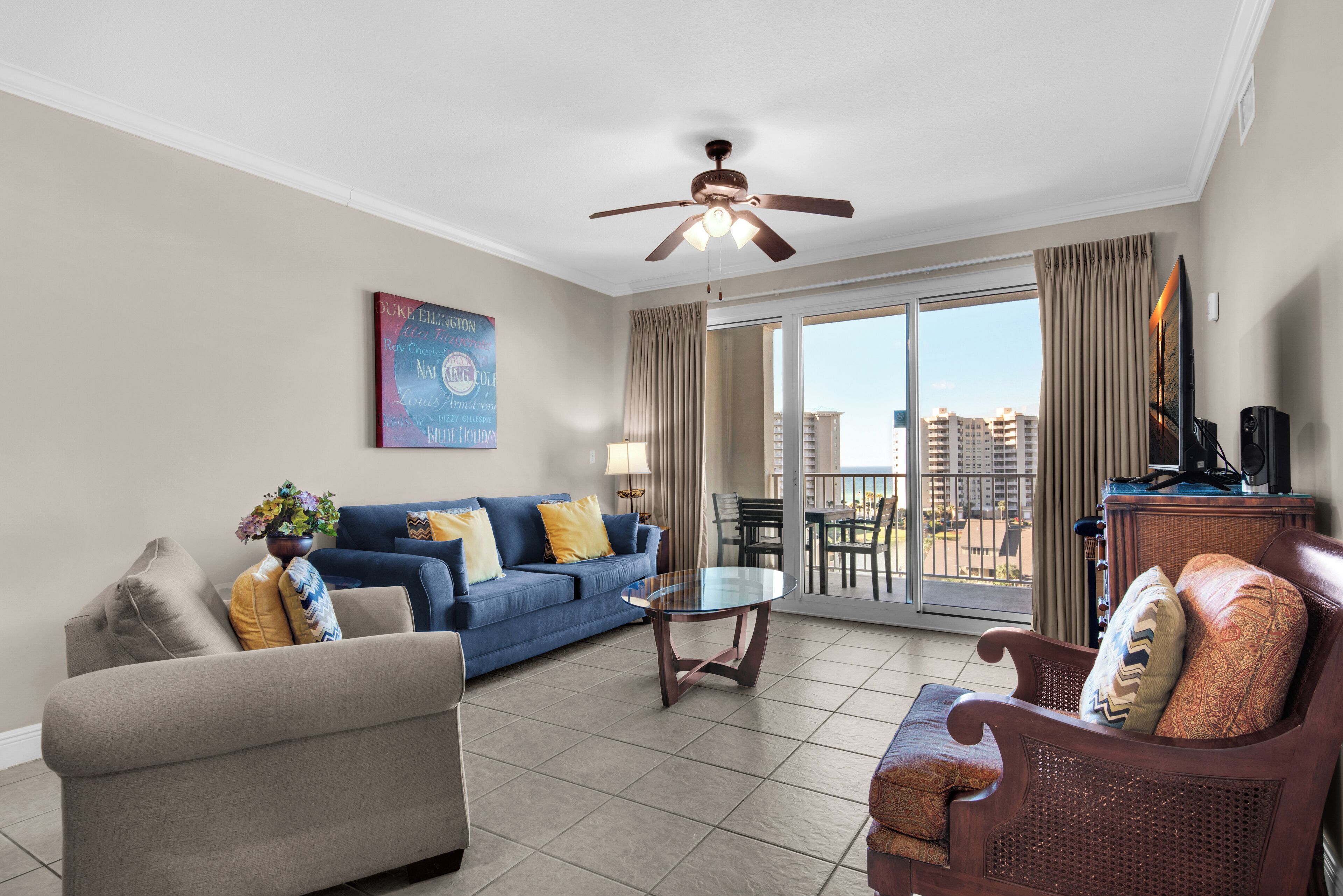 A modern living room with a sofa, armchair, and coffee table, a ceiling fan, and a large window with a city view.
