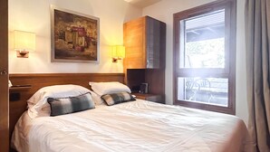Una camera d'albergo con un letto, un quadro appeso al muro, una finestra con tende e un comodino con una lampada.